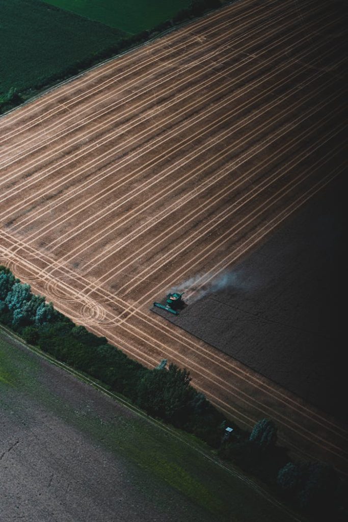 Drone captures a combine harvester working across a large rural field during harvest season.
